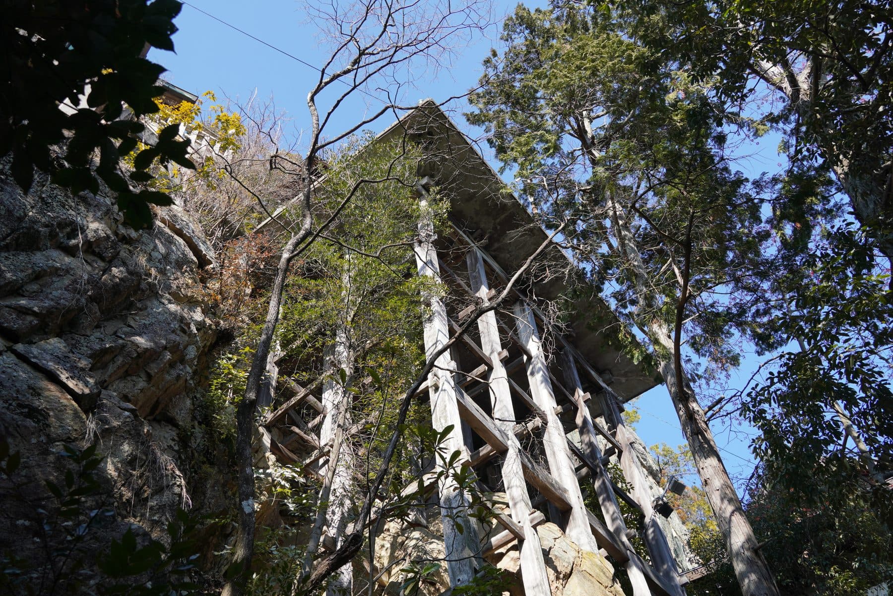 太郎坊宮の舞台を真下から見上げた様子。断崖の岩の上に木の柱が井桁状に組まれ、その上に床が架かっている